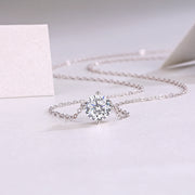 A classic round-cut moissanite stone necklace with a four-prong setting, displayed against a white background.